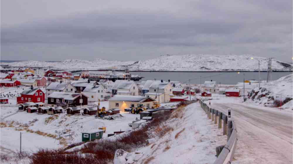 This image shows a tiny fishing community with red colored houses next to the arctic ocean during wintertime with snow, in northern Norway called Bugoynes.