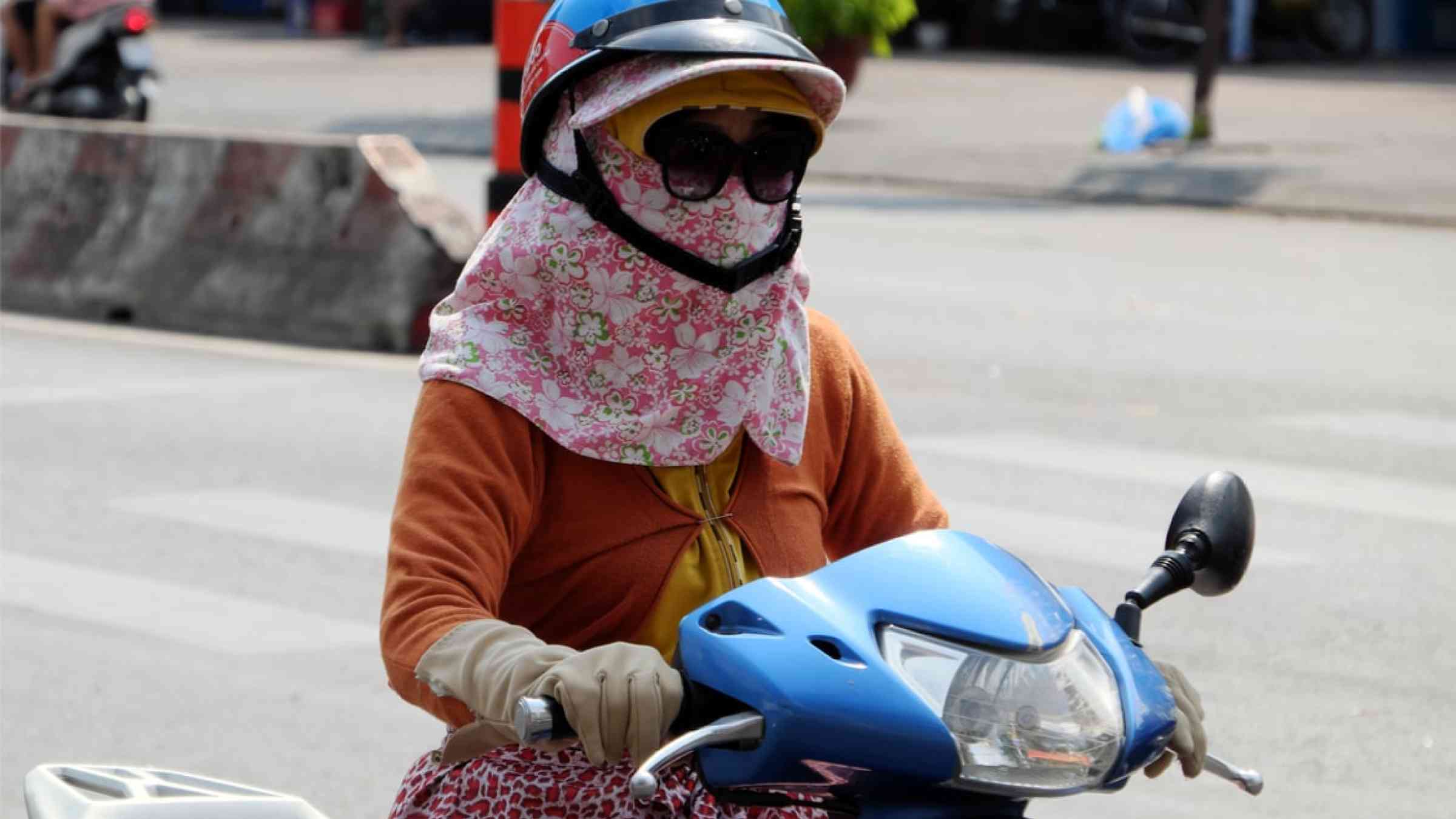Vietnamese woman wear glasses, face mask, coat, gloves to sun protection, ride motorbike under high temperature in Ho Chi Mihn City, Vietnam (2019)