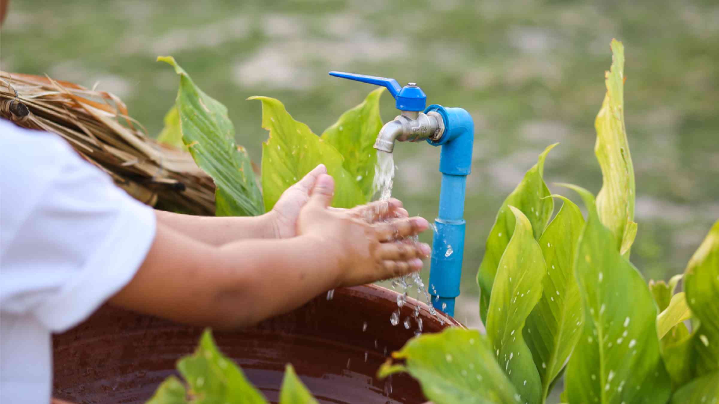 An Asian boy washes his hand at an outdoor sink and a water carton.