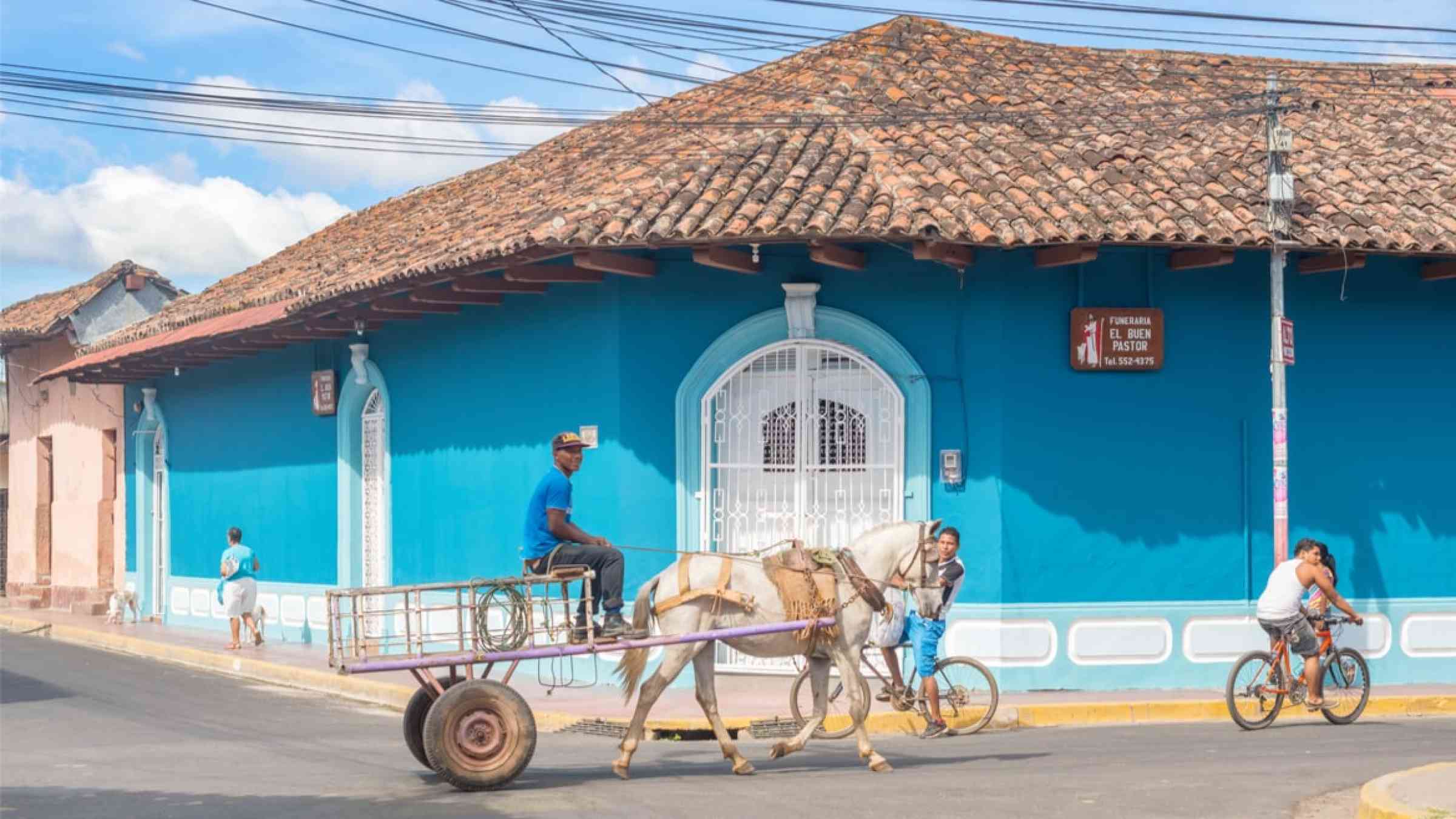 People riding bicycles on the street of colorful commercial houses in the historic district of Granada, Nicaragua