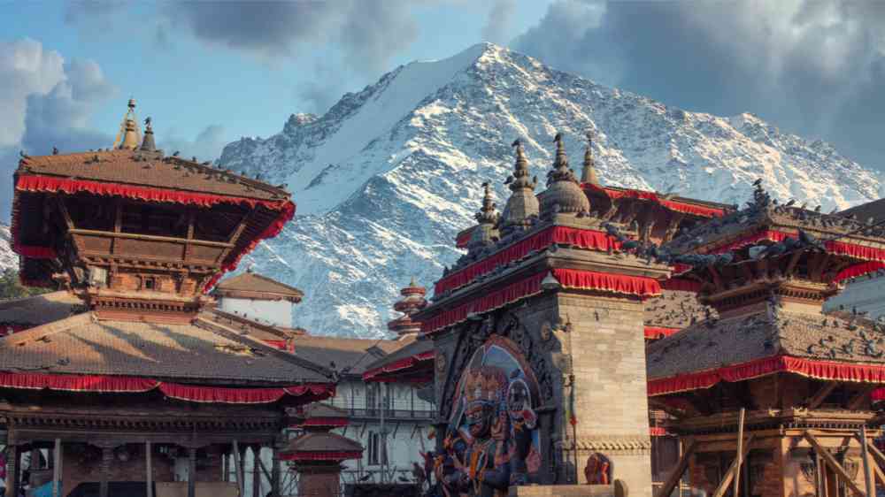 This image shows a city in Nepal below a snowy mountain.