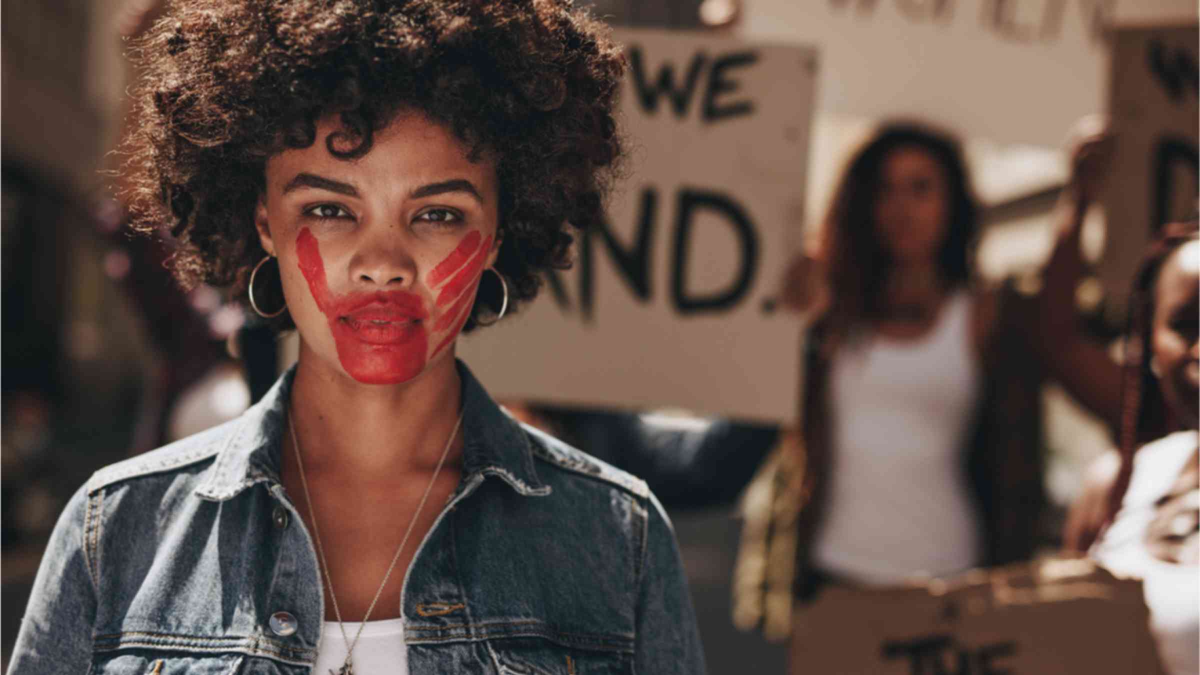 African woman with red hand on her mouth during a protest. Group of activists demonstrating to stop abuse of women.