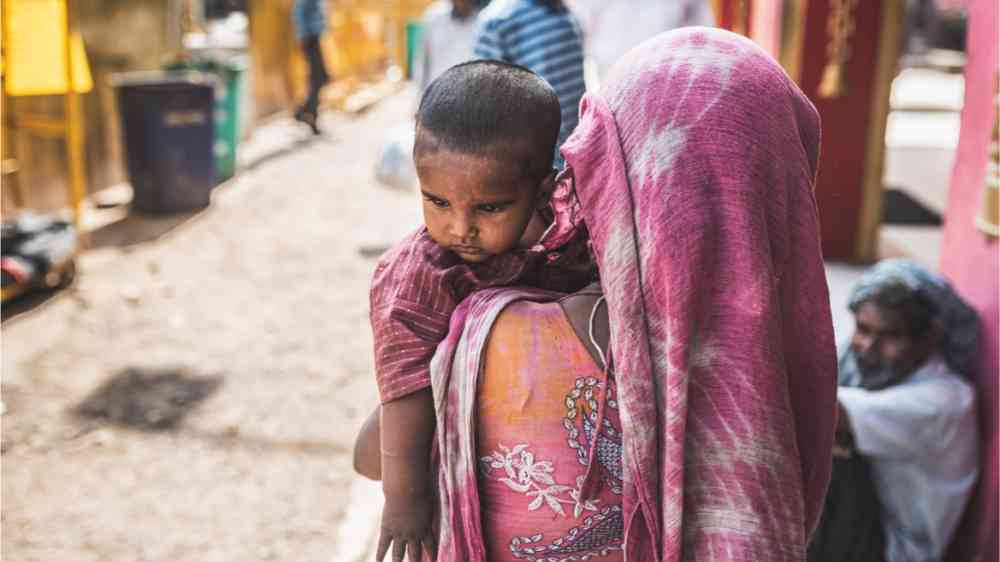 A woman carrying a child through the heated streets.