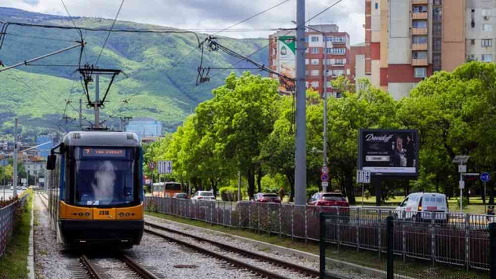 A yellow and black train on train tracks going through a city.