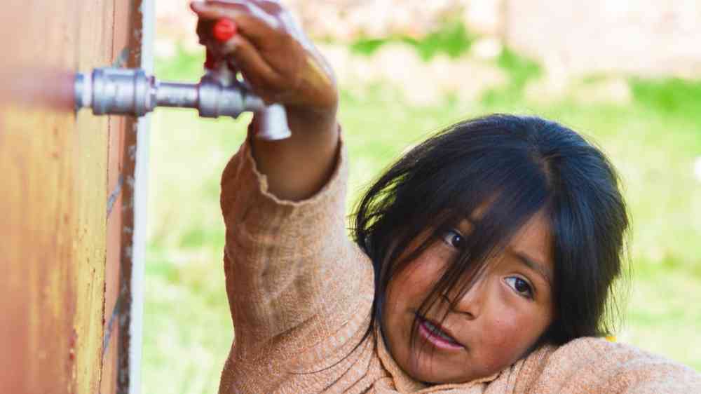 A little girl trying to open a water tap in Mexico.