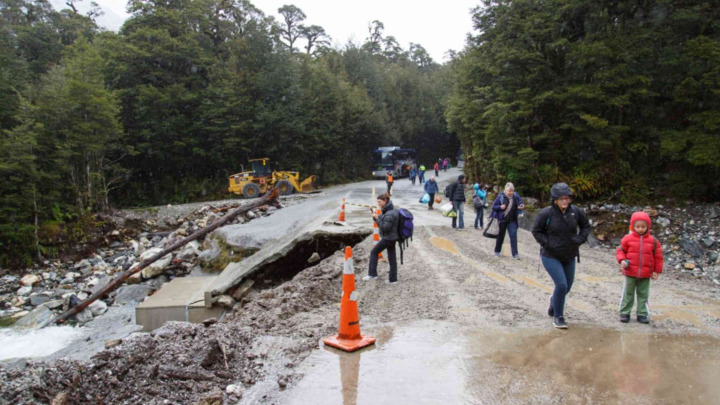 People walk along the road because the road has been washed away by torrential rain causing flooding and road collapse.