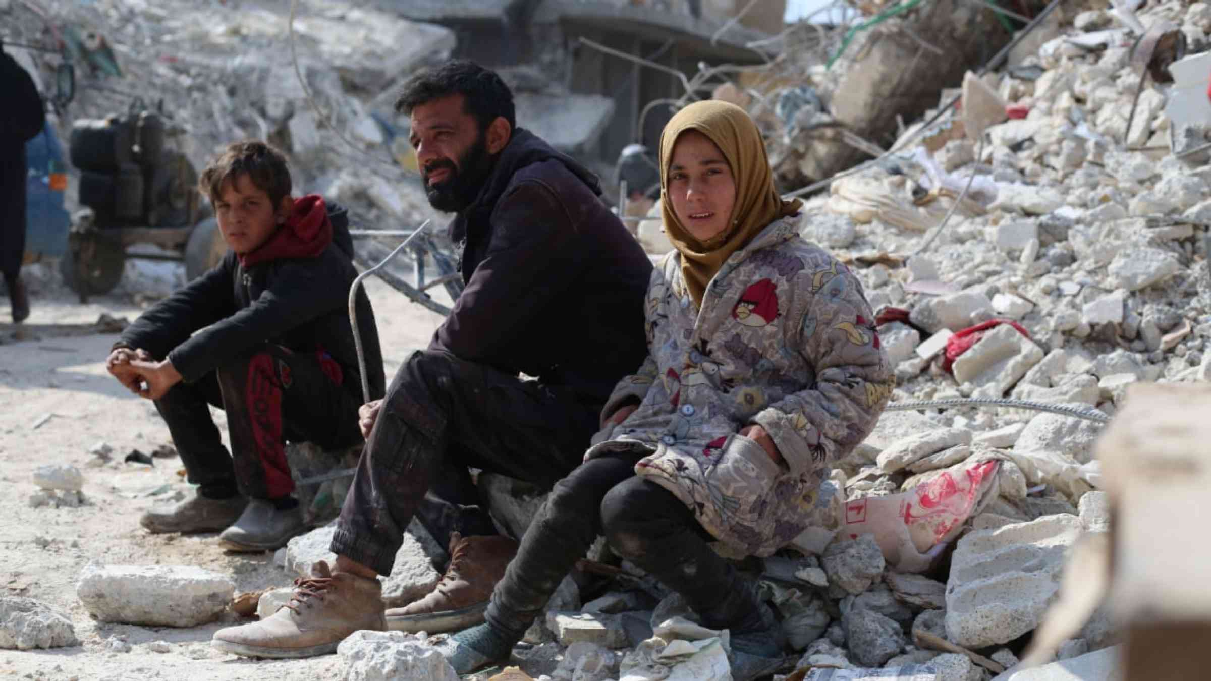 Three Syrian people sitting on the rubble in Aleppo after the earthquakes struck in 2023.