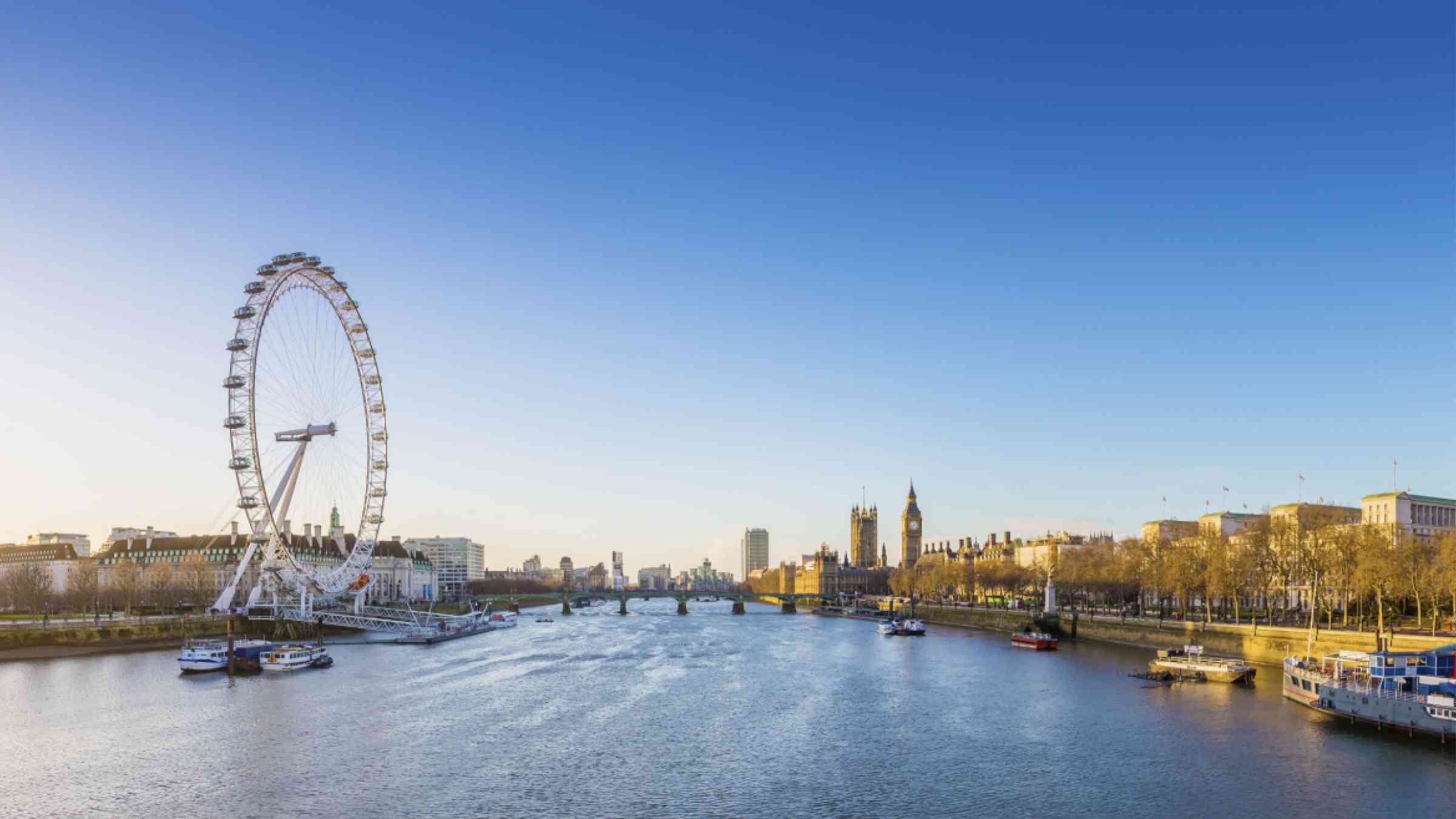 London skyline view at sunrise with famous landmarks, Big Ben, Houses of Parliament and ships on River Thames with clear blue sky