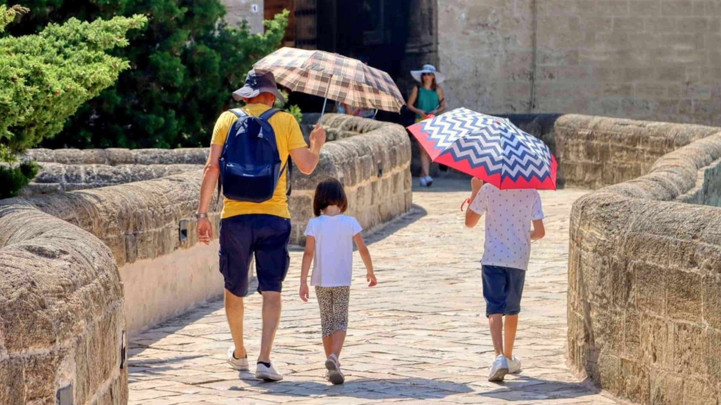 Father protects his children with umbrellas from the sun on a very hot day.