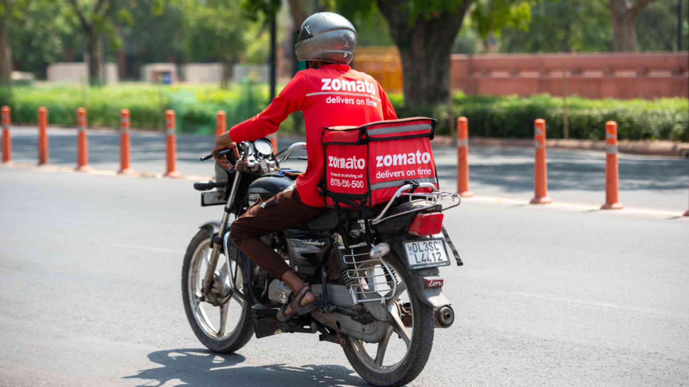 Delivery employee riding motorcycle on a road in New Delhi, India, 2024