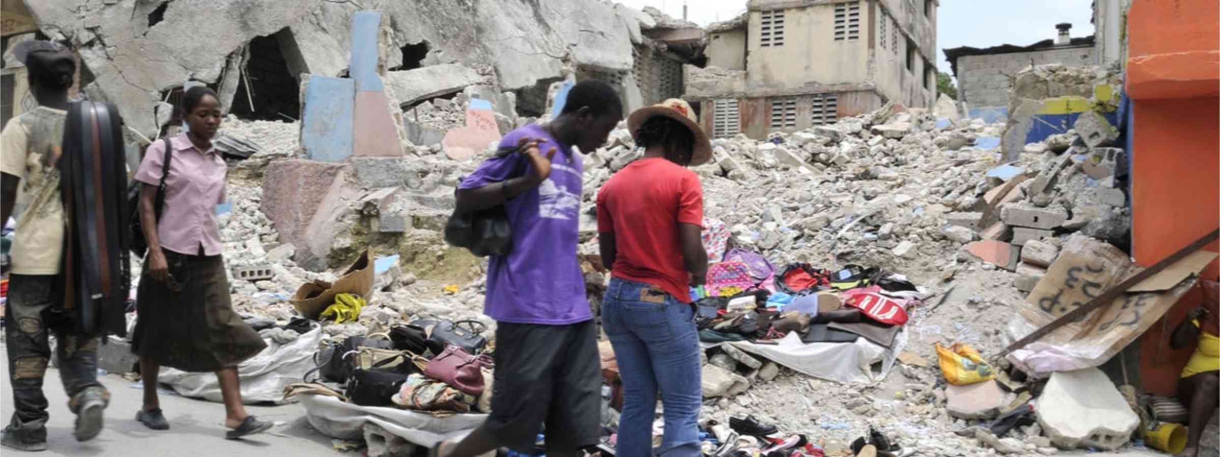 Two people standing in front of a collapsed building after the Haiti earthquake in 2010.