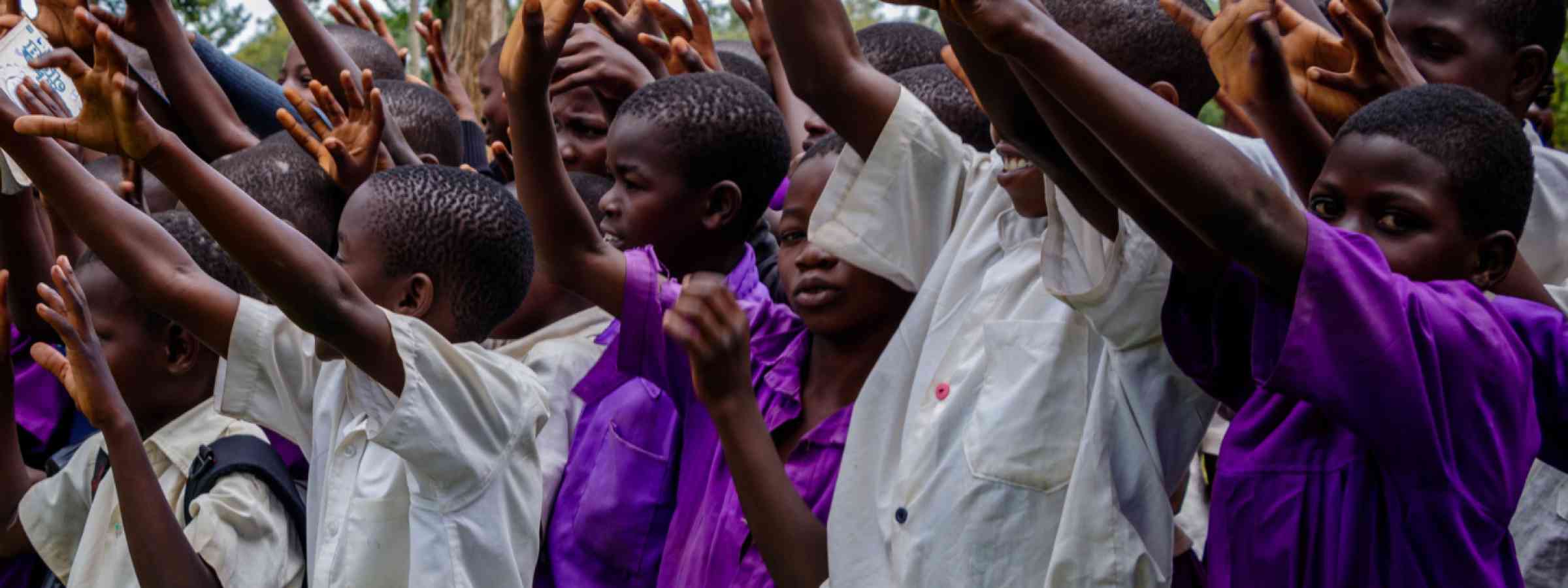 School chlidren at a primary school in Uganda lifting their hands.